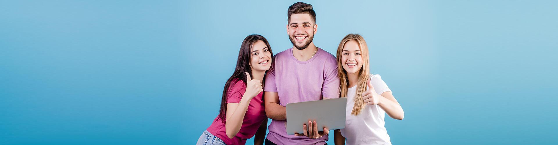 drei junge Menschen, stehend, Mann in der Mitte hält Laptop in der Hand